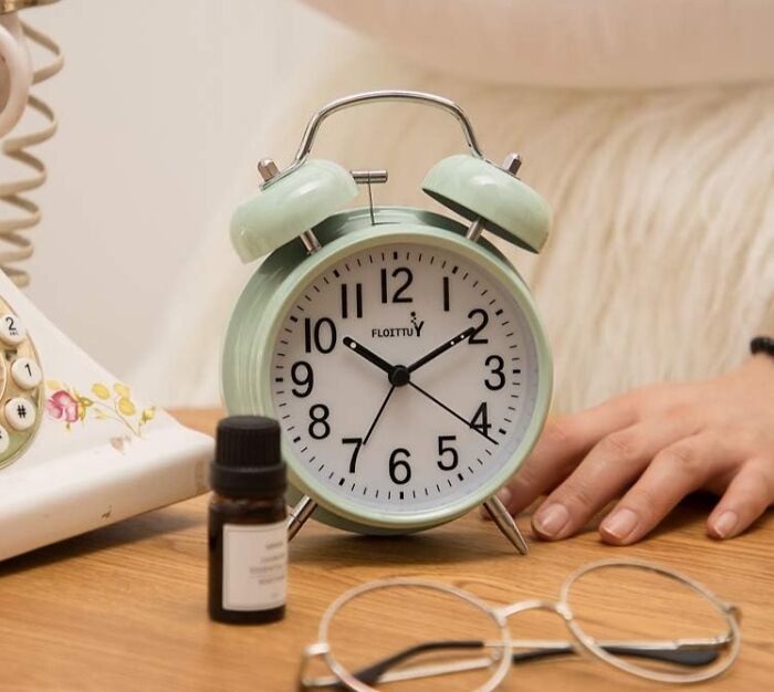 Retro alarm clock on wooden table with glasses, symbolizing a digital detox moment.