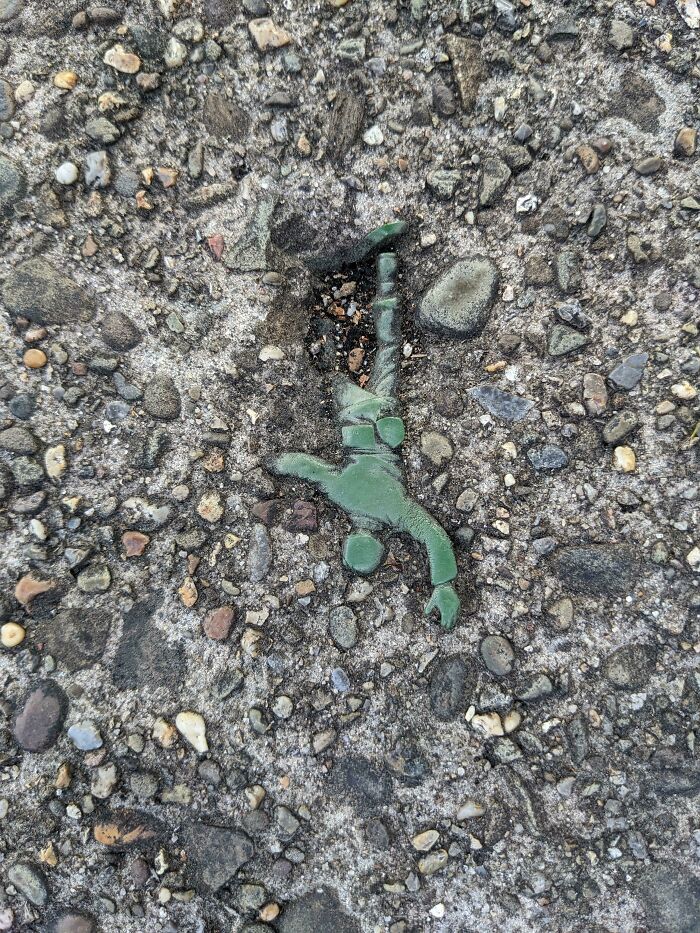 Green toy soldier partially embedded in rough concrete, showcasing Time vs. Things in urban decay.