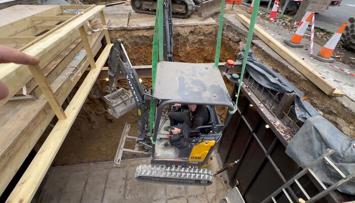 Worker operating excavator in deep construction site, illustrating employees blatantly ignoring safety protocol risks.