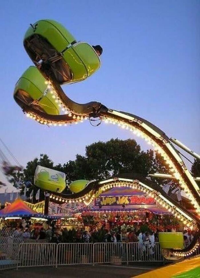 Nostalgic carnival ride with green seats lit by bulbs against evening sky, crowds visible at a fairground event.