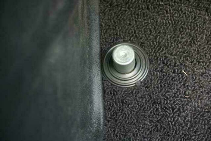 Close-up of an old car's carpeted floor with a vintage locking pin, evoking nostalgic memories of past decades.