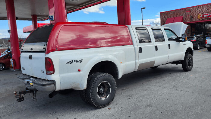 Modified white 4x4 truck with extended bed and red camper shell showcasing redneck engineer creativity.