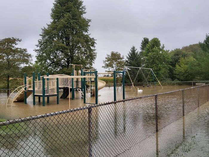 Flooded playground showing nature's powerful impact, with water submerging swings and slides.