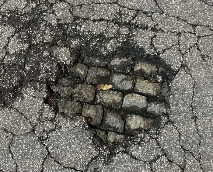 C*****d asphalt revealing cobble stones beneath, illustrating time's effect on things.