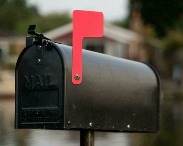 Black mailbox with raised red flag in a suburban setting, evoking nostalgic feelings of old-fashioned mail delivery.