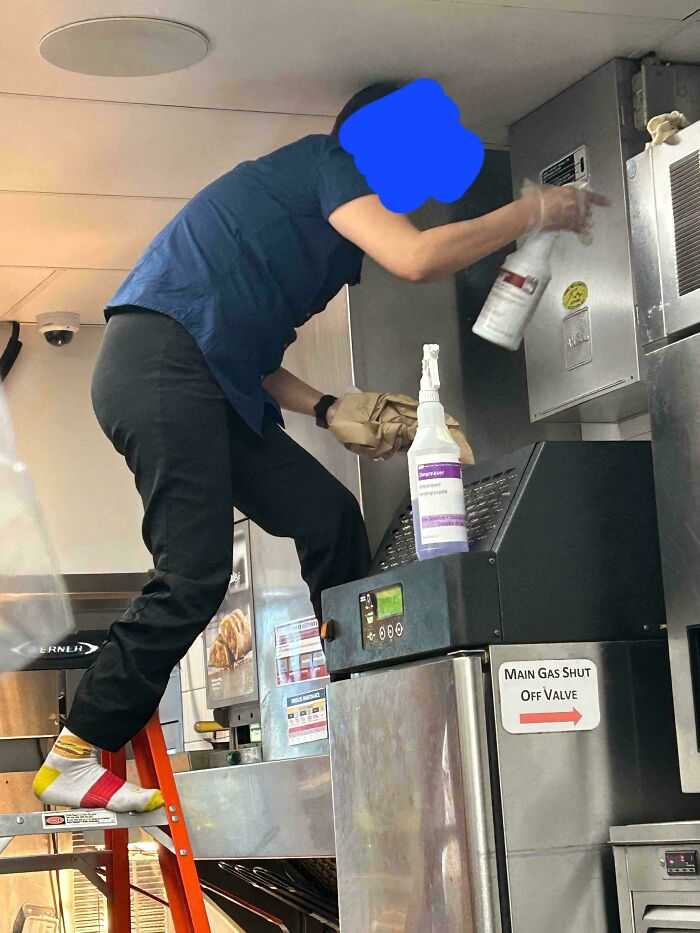 Employee ignoring safety protocol standing barefoot on ladder near industrial kitchen equipment, risking dangerous accident.