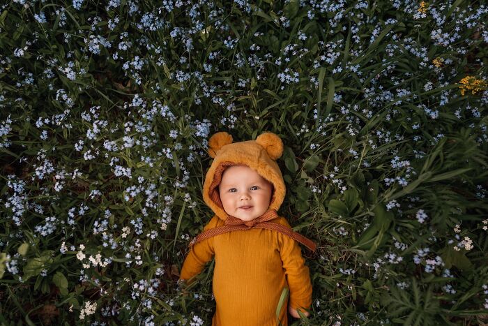 Baby in bear outfit lying on a bed of wildflowers, capturing the magic of childhood.