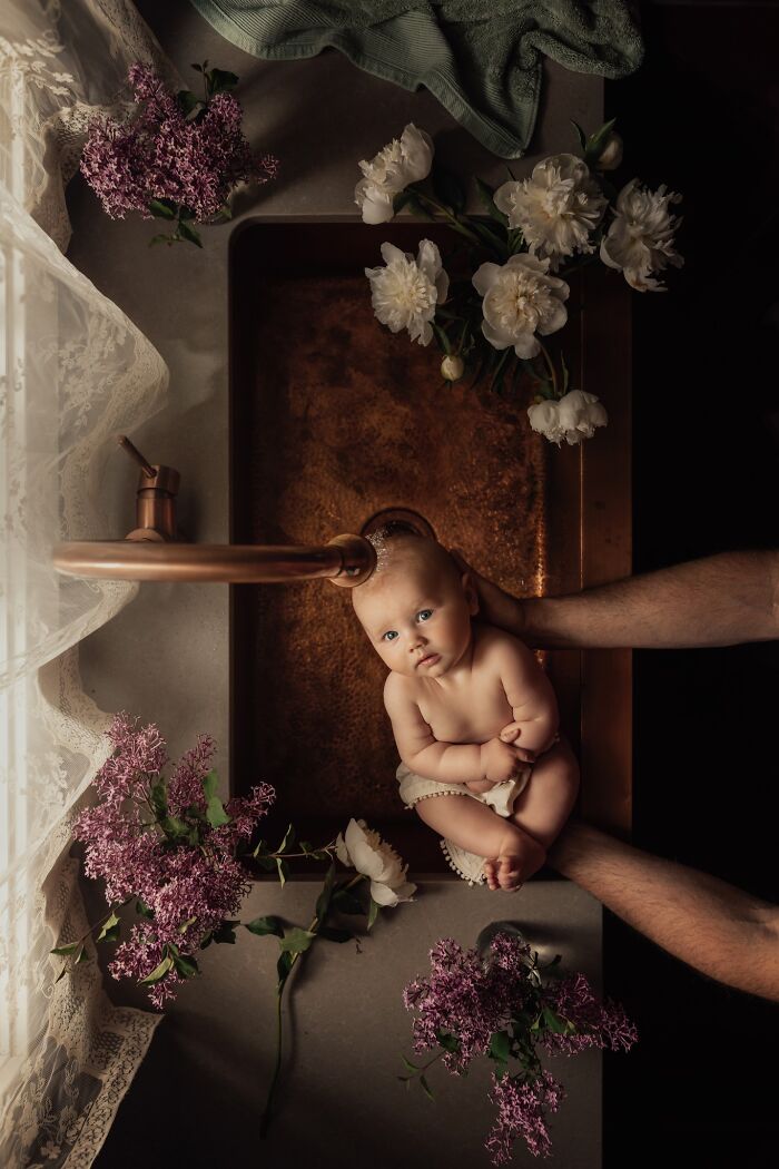 Baby sitting in a sink surrounded by flowers, capturing the magic of childhood through a mother's lens.