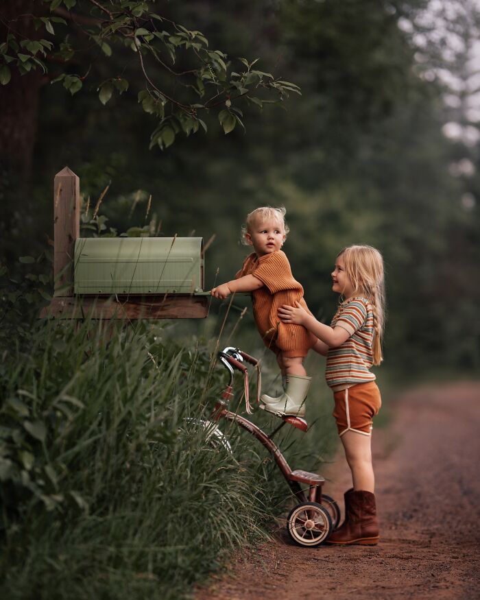 Children exploring nature together, with a small child reaching a mailbox assisted by an older sibling, capturing the magic of childhood.
