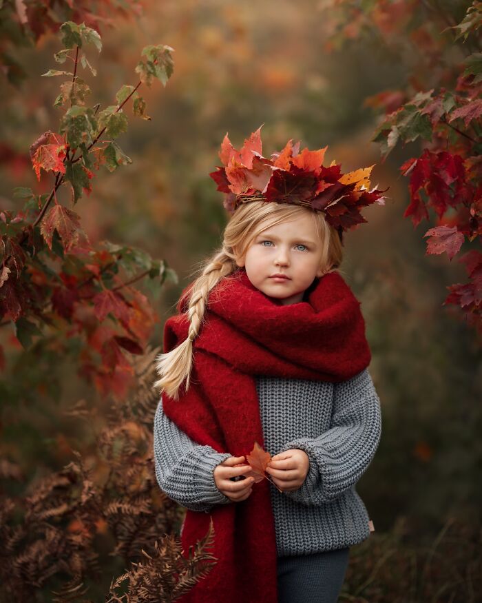 Child in autumn attire with leaf crown and red scarf, capturing childhood magic in nature.