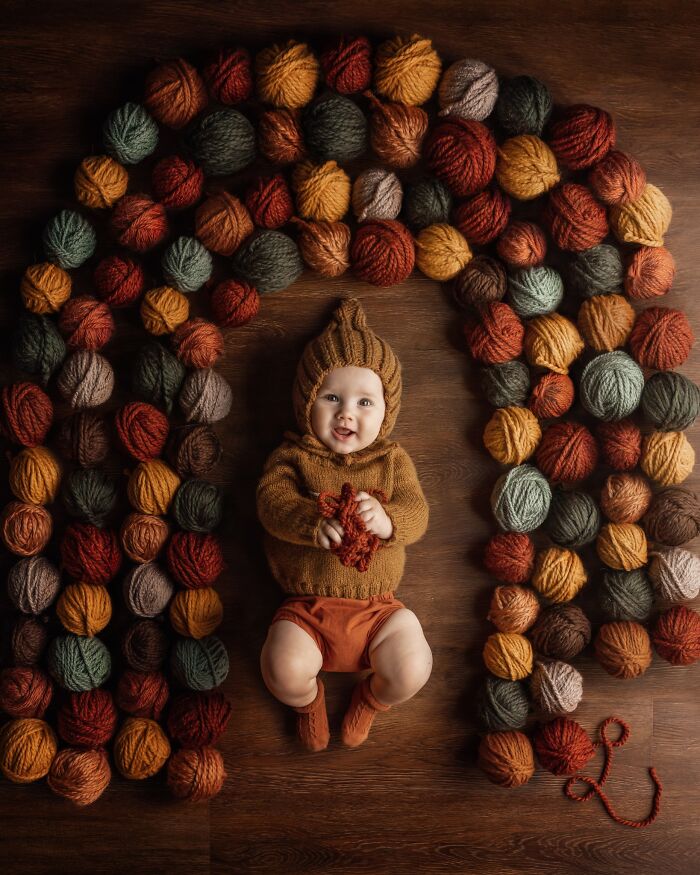 Baby in cozy knit outfit surrounded by colorful yarn balls, capturing the magic of childhood.