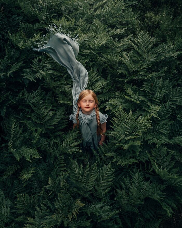 Child enjoying nature, wrapped in a scarf, surrounded by lush green ferns, capturing the magic of childhood.