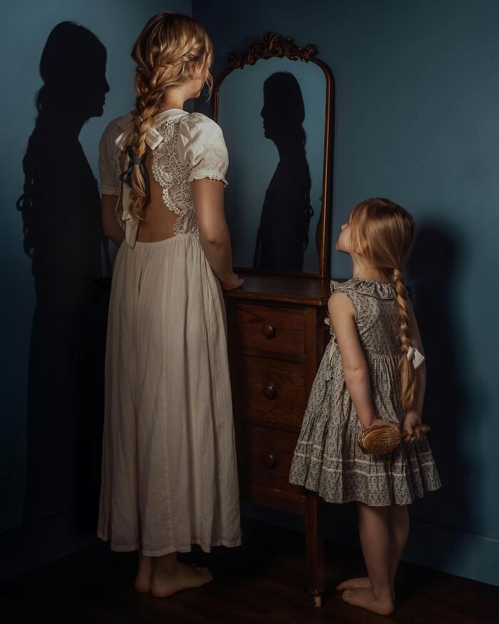 Childhood magic captured by mother; two girls with braided hair looking in a mirror, shadows reflecting on the wall.