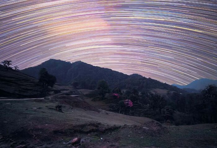 Star trails creating mesmerizing patterns over a hilly landscape at night, showcasing astrophotography brilliance.
