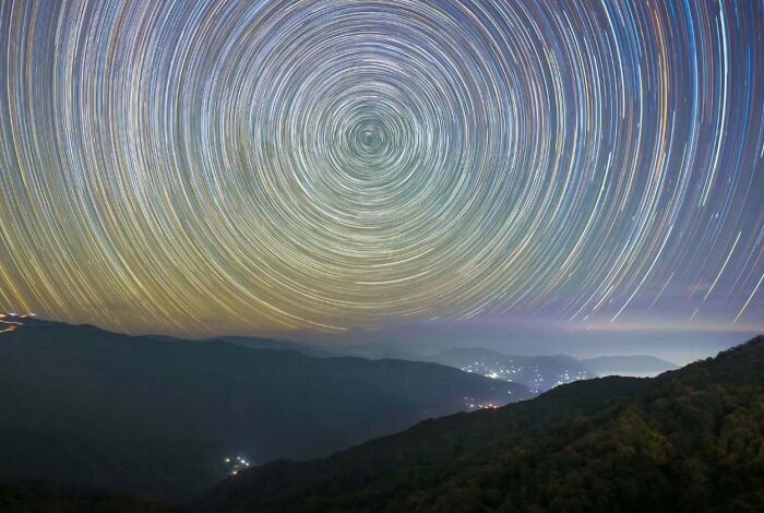 Star trails over a mountainous landscape, showcasing mesmerizing astrophotography of the night sky.