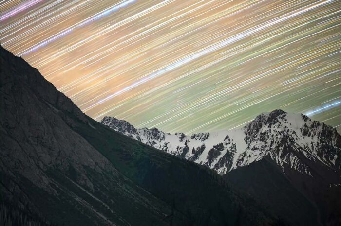 Astrophotography of snowy mountain peaks and vivid star trails in the night sky.