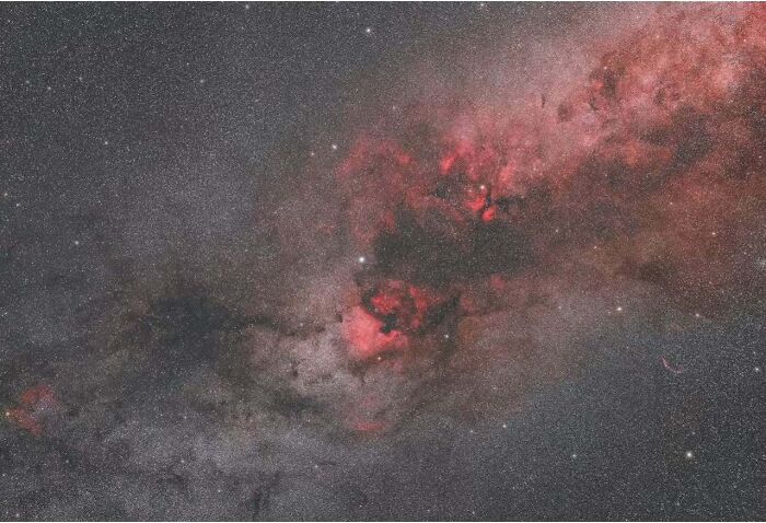 Astrophotography capturing vibrant red nebula set against a starry night sky.