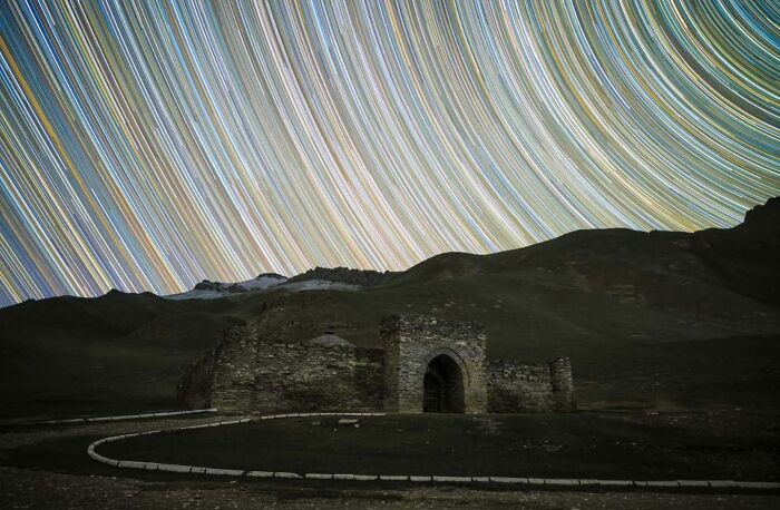 Ancient ruins under swirling star trails in a night sky, showcasing mesmerizing astrophotography.