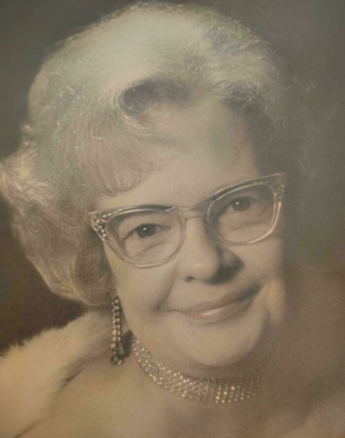 Elderly woman wearing glasses and vintage jewelry, offering a candid glimpse into the past with a warm smile.