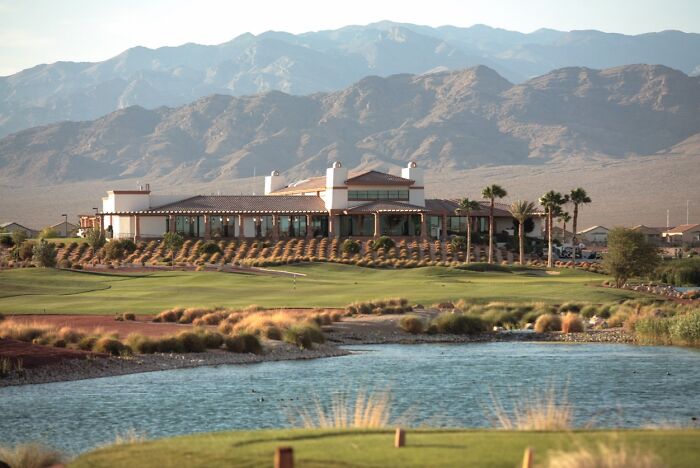 Breathtaking golf course with mountains in the background and a clubhouse by a water hazard.