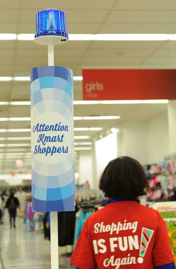 Blue alert light in store with retro sign and employee wearing red shirt with nostalgic shopping message inside Kmart.