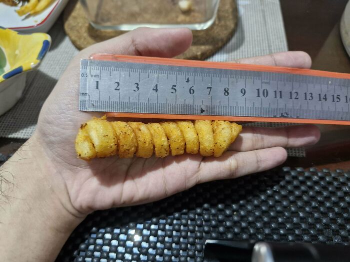 Ruler measuring a curly fry in a hand, highlighting mundane everyday objects.