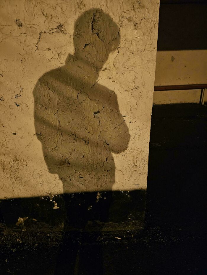 Shadow of a person on a textured wall under orange lighting, featuring nothing interesting.