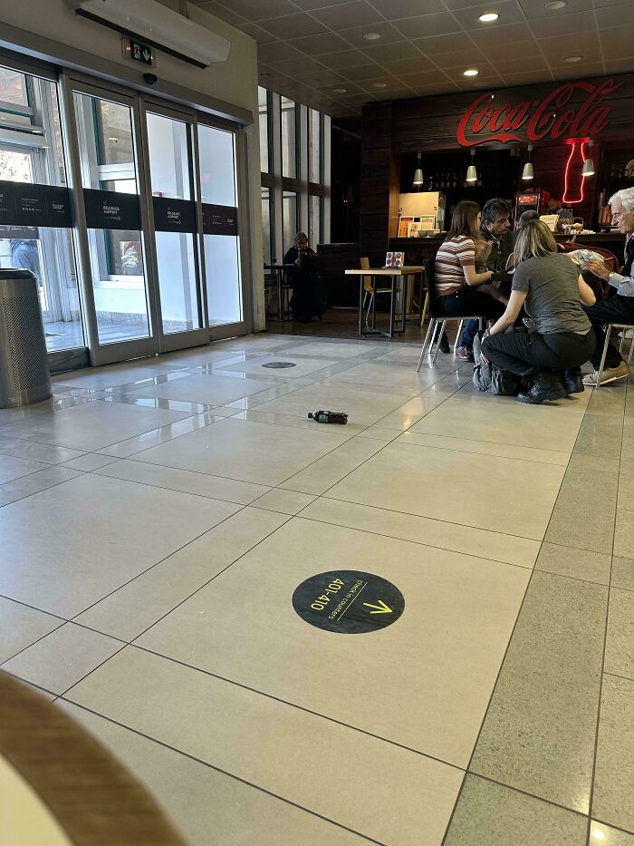 Empty cafe floor with a small object, people dining in the background, Coca-Cola sign visible.