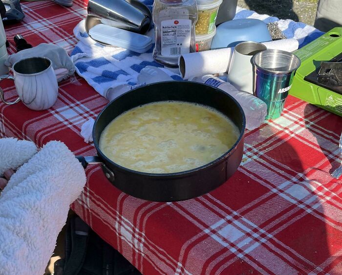 Plain table with a pan of scrambled eggs and various items scattered around.