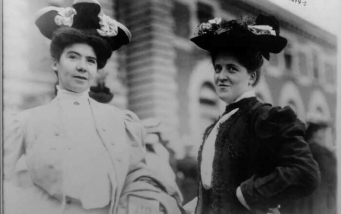 Two women in early 20th century fashion wearing elaborate hats in a candid glimpse into the past photograph