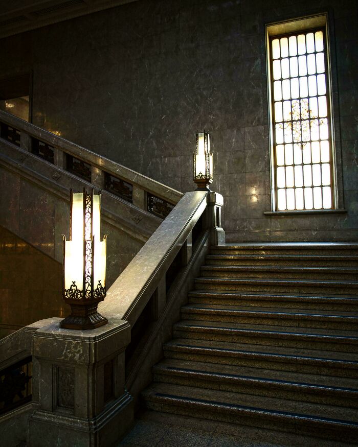 Elegant marble staircase with ornate lamps and a tall window showcasing impressive architectural feats.