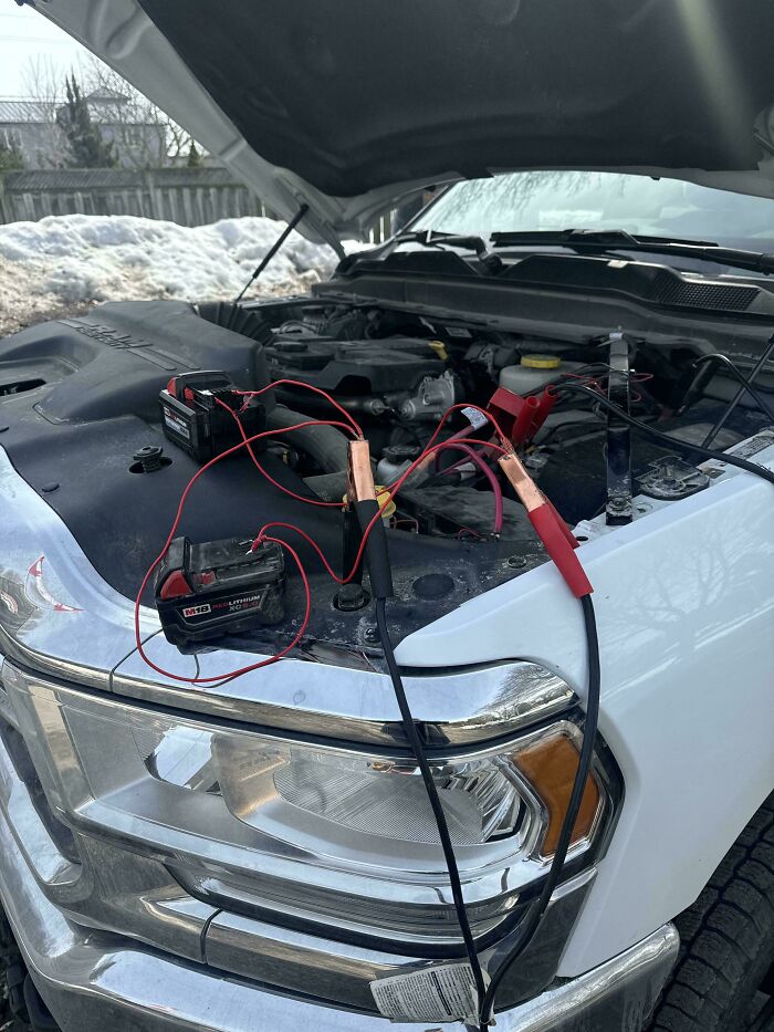 Improvised redneck engineer battery setup with jumper cables and power tools on a truck in a snowy outdoor setting.