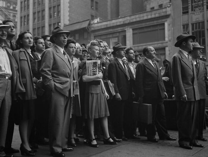 Group of people in 1940s attire standing on city street, showcasing candid glimpses into the past with vintage fashion and expressions.