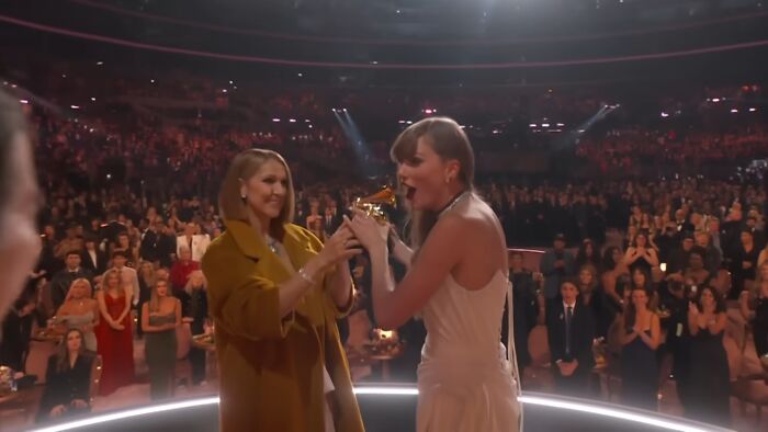 A surprising moment at an awards show, a woman in a white dress receives a trophy, audience in the background.