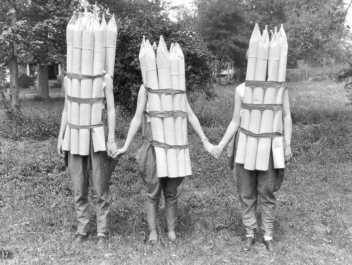Three people wearing ridiculous pencil costumes, holding hands in a grassy area.