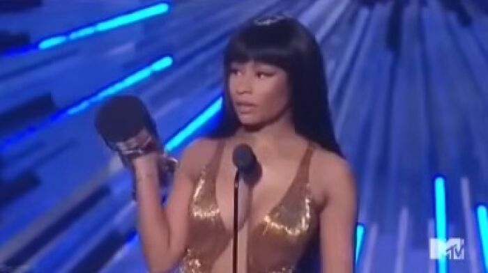 Person holding an award at an MTV event, wearing a gold dress, during a scandalous moment on stage.