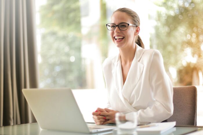 Smiling woman in glasses at a desk with a laptop, discussing overused office expressions.