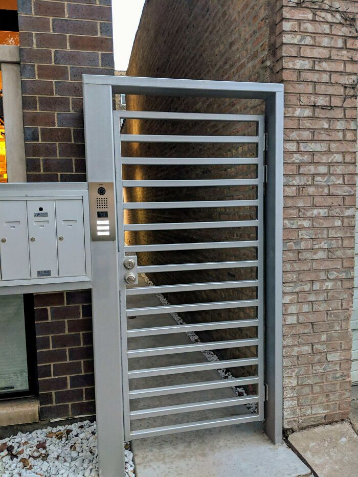 Metal gate design with open bars, positioned next to mailboxes, leading to a narrow alley; an example of disastrous designs.