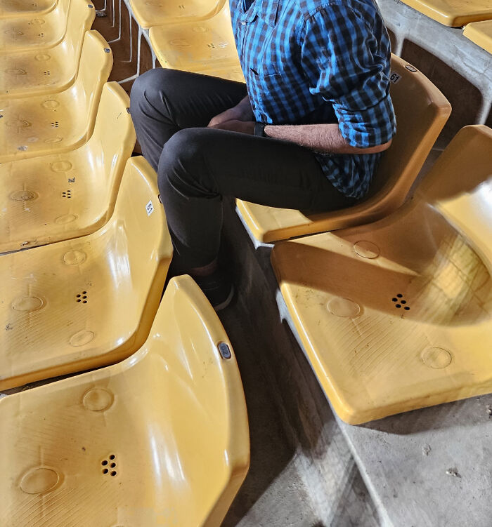 Person awkwardly seated on badly aligned stadium chairs, showcasing a disastrous design.