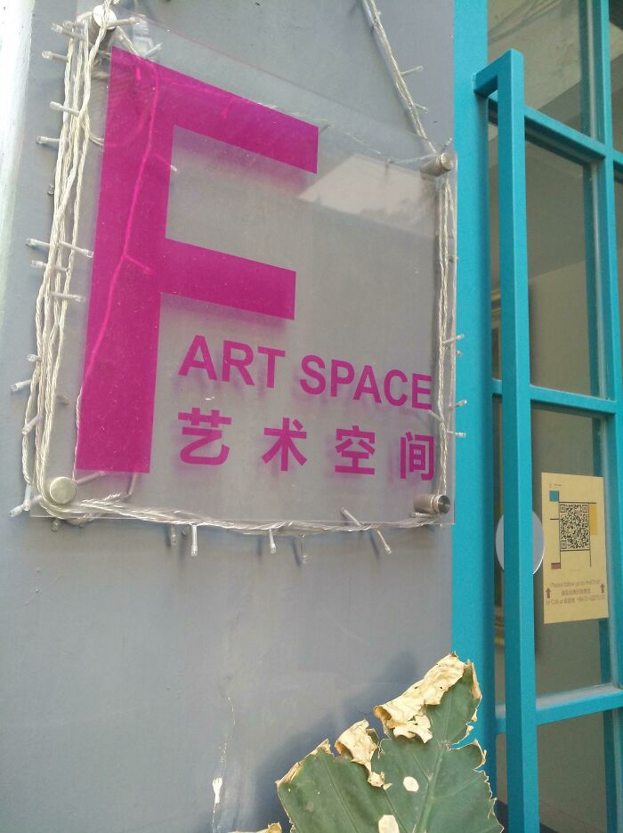 Sign reads "F ART SPACE" in pink, showcasing a disastrous design on a gray wall next to a green door.