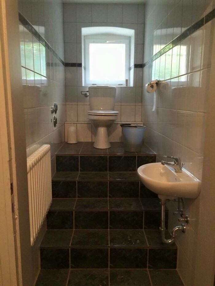 Bathroom design with a toilet elevated on tiled steps, featuring a small sink and window.