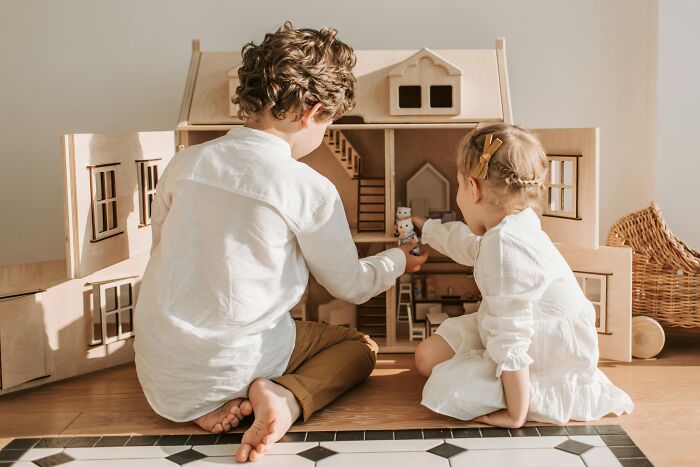 Two children playing with a wooden dollhouse, challenging common stereotypes through imaginative play.