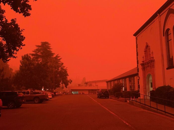A street under an intense red sky from wildfire smoke, capturing the world's awe-inspiring phenomena.