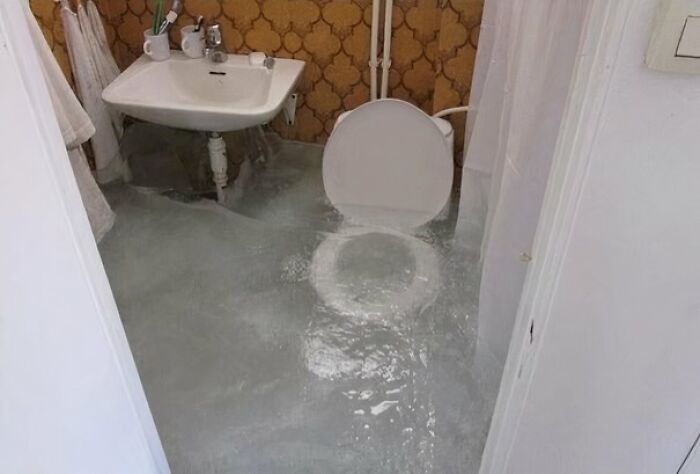 Flooded bathroom with poor design decisions, showing standing water around a toilet and sink.