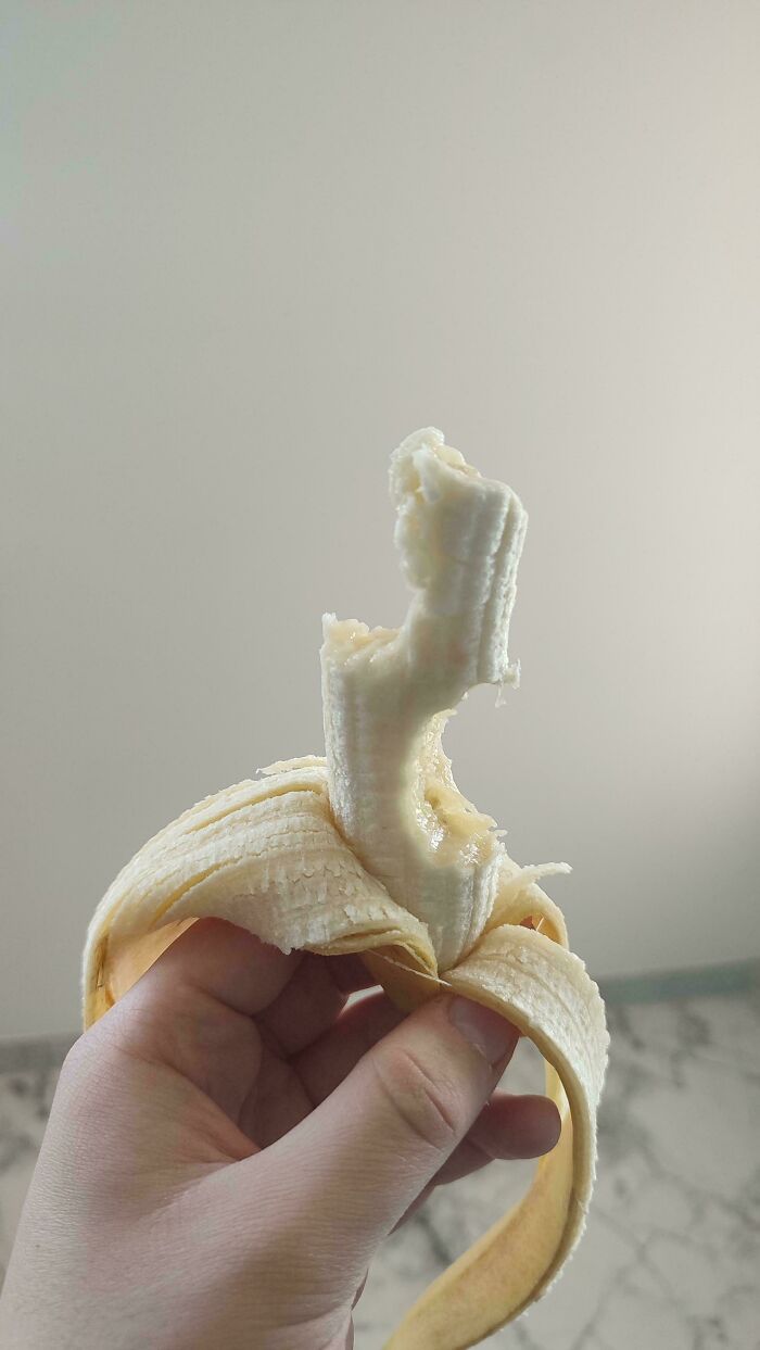 Hand holding a half-peeled banana against a plain background.