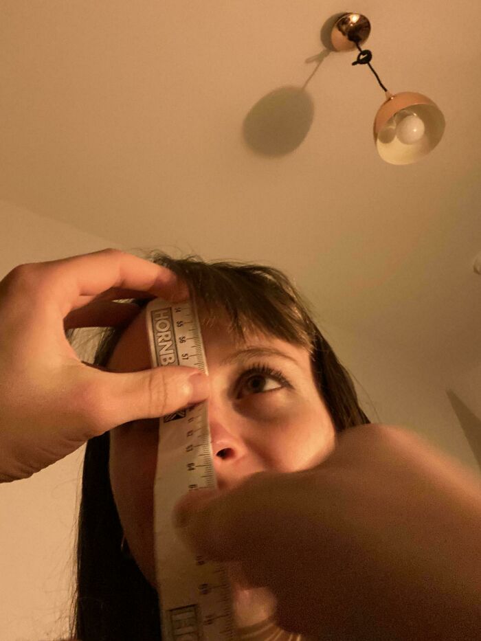 Person measuring their face with a ruler under a simple ceiling light.