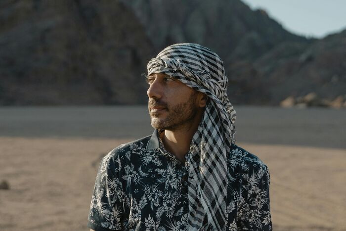 Man in a patterned shirt and headscarf standing in a desert, representing challenging common stereotypes.