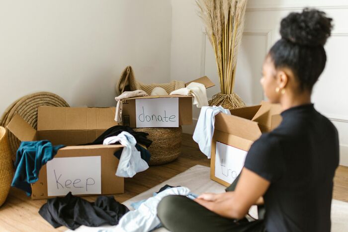 Person sorting clothes into boxes labeled keep, donate, and trash, addressing common stereotypes on decluttering.