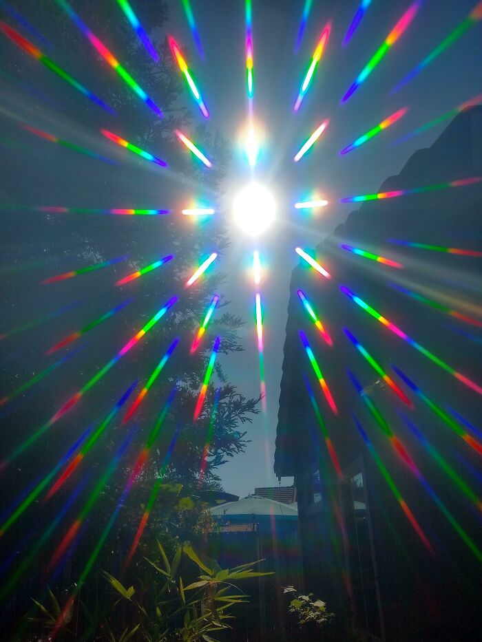 Colorful light beams radiate from a bright sun, creating a vibrant spectacle against a clear sky.