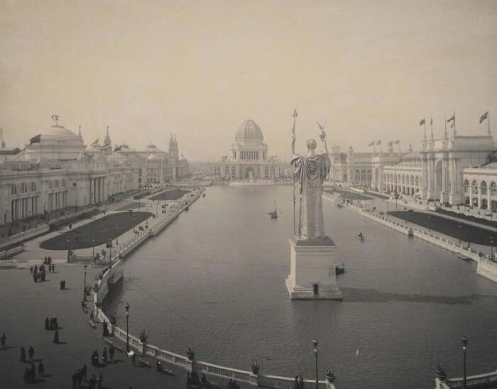 Historic American architecture featuring a grand statue overlooking a reflecting pool with buildings and flags in the background.